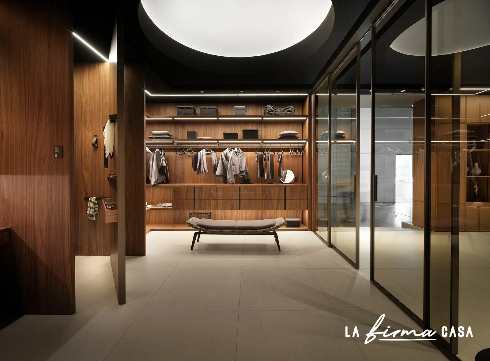 Walnut walk in closet with glass pivot door by Barausse in Canada