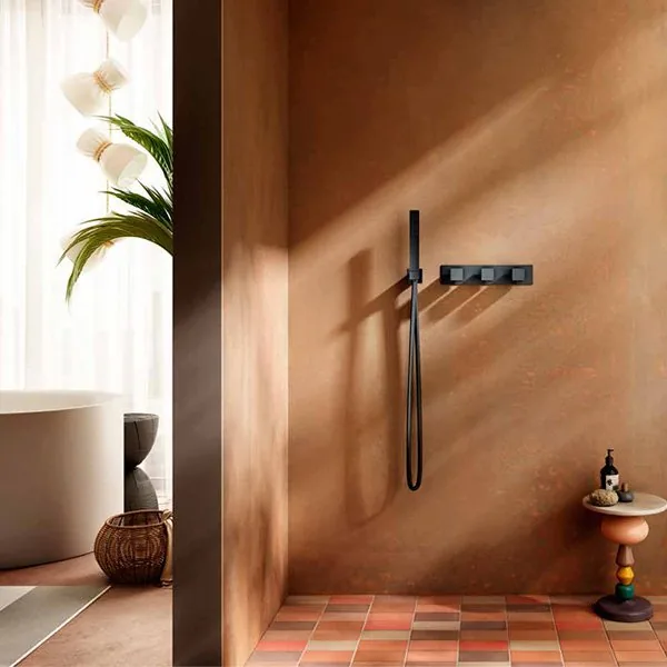 Aquaelite matte black handshower and thermostatic control bar on a terracotta plaster wall above checkerboard tiles, with a freestanding tub beyond the partition