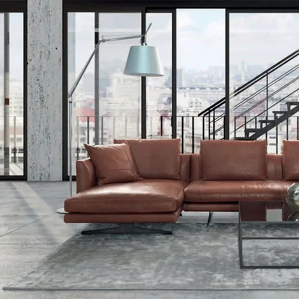 Gyform tan leather sectional sofa on a grey rug in a loft with full-height windows, an arc floor lamp and a black steel staircase
