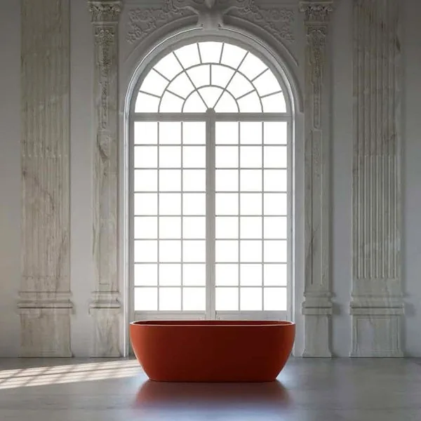 IW&W terracotta freestanding bathtub in front of a tall arched window, between fluted marble pilasters in a pale stone hall