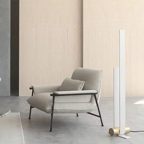 Lenzi Home cream bouclé armchair on a slim black frame beside a tall white floor lamp, against a pale ash panelled wall