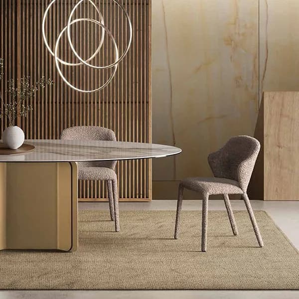 Tafaruci oval marble dining table on a sculptural champagne base with bouclé chairs, beneath interlocking ring pendant lights against a slatted wood and onyx wall