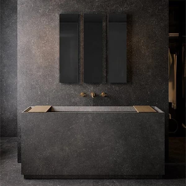 TerzaDimensione dark stone bath surround with brass wall taps and three tall black mirror panels against a ribbed stone wall