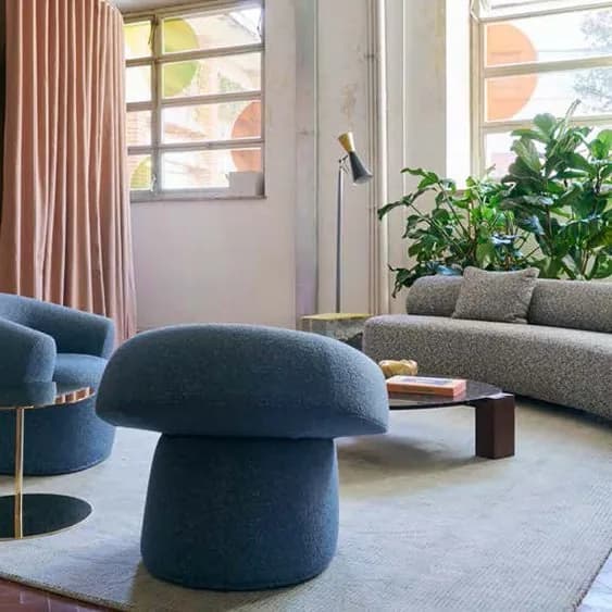Warli blue bouclé mushroom pouf and matching swivel armchair beside a grey sofa on a pale rug, in a loft with tall windows